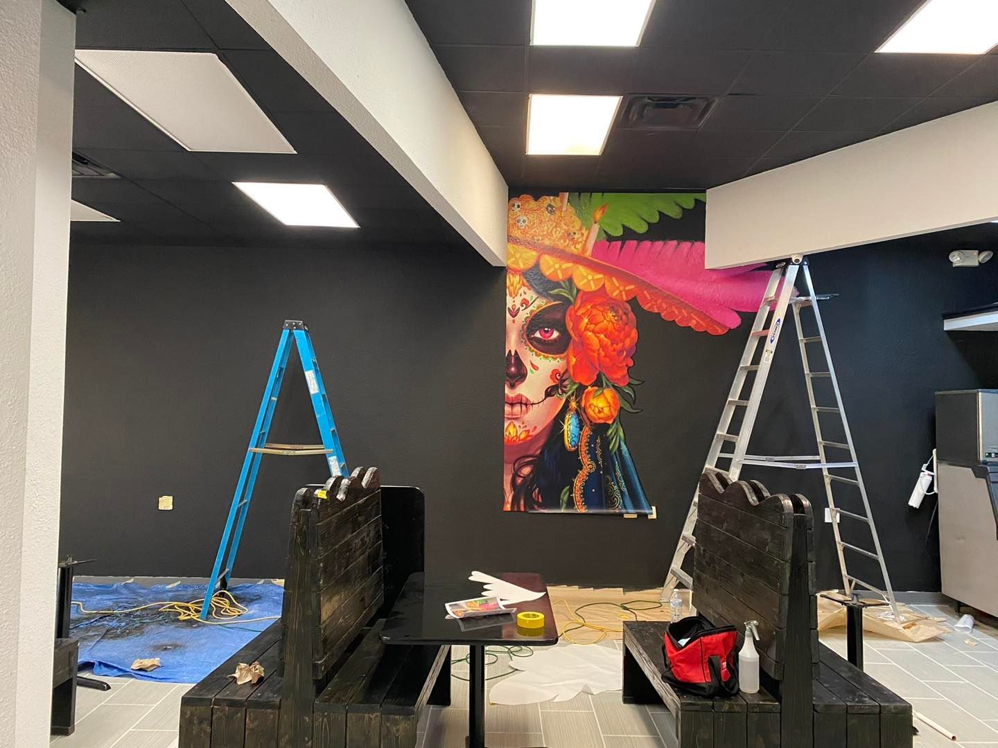 Empty room under renovation with ladders, paint supplies, and a colorful mural on the back wall