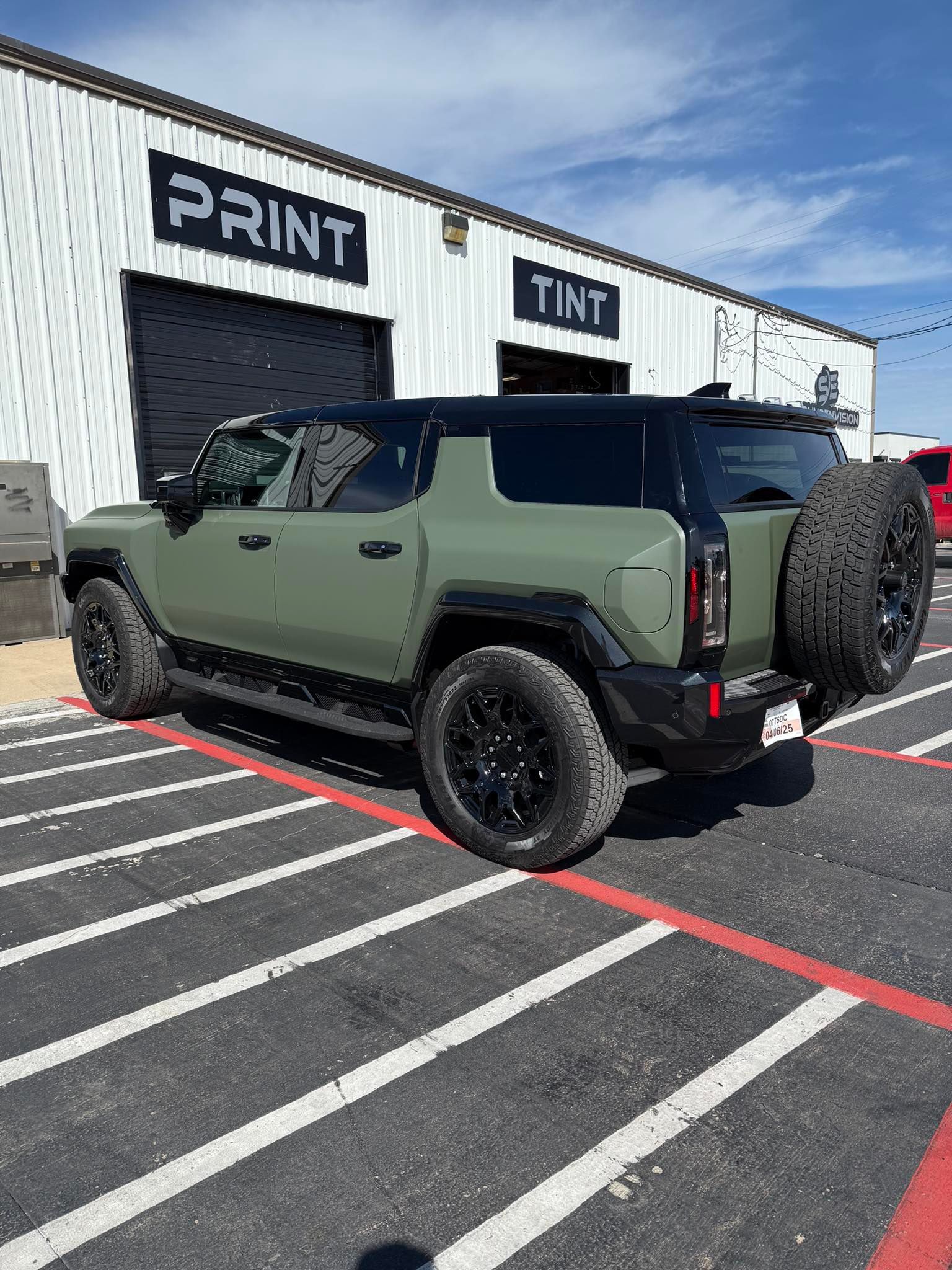 Green off-road SUV parked in front of a print shop on a sunny day