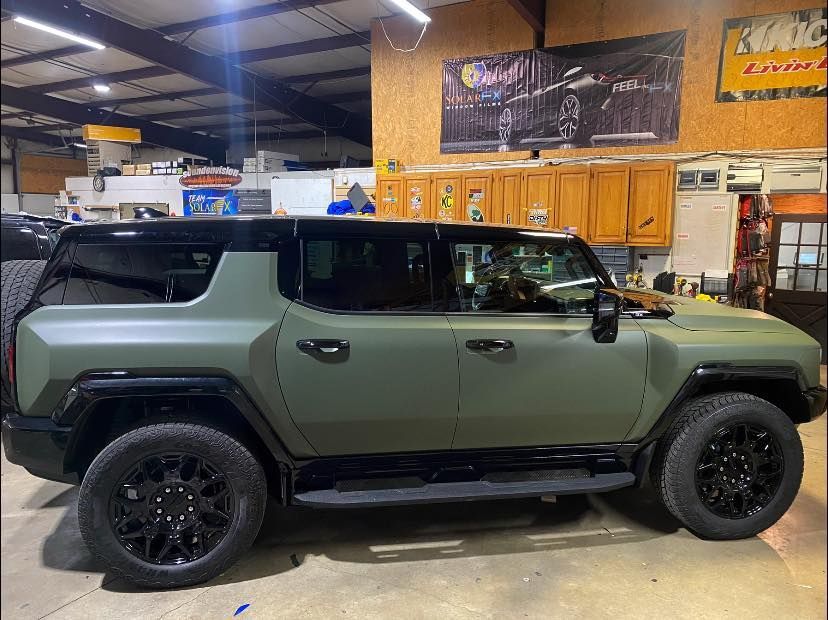 Olive green off-road SUV with black wheels parked inside a garage or workshop.