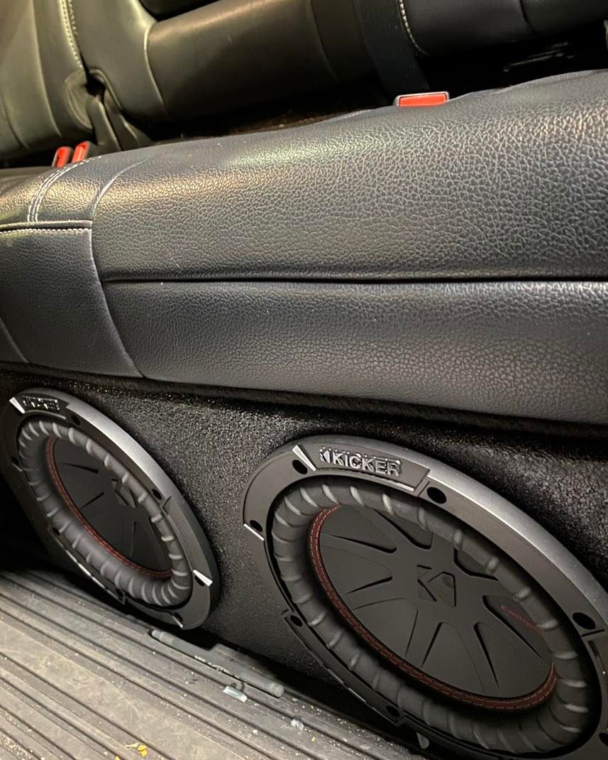 Black car interior with two round subwoofers mounted below the rear seat.
