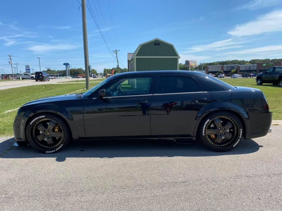 Black sedan parked on pavement under clear sky, side view with dark wheels and tinted windows.
