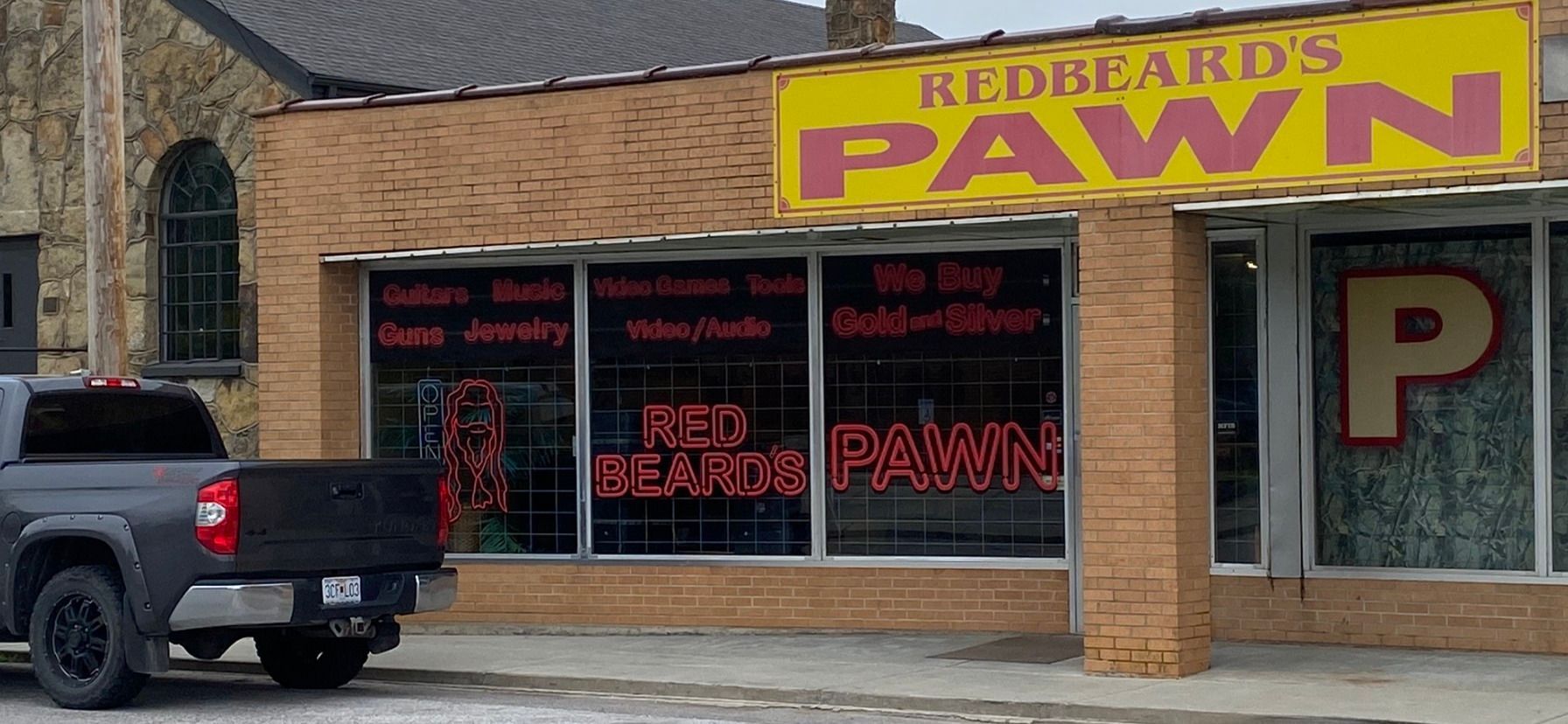 Red Beard’s Pawn storefront with yellow sign, red window lettering, and a black pickup truck parked outside