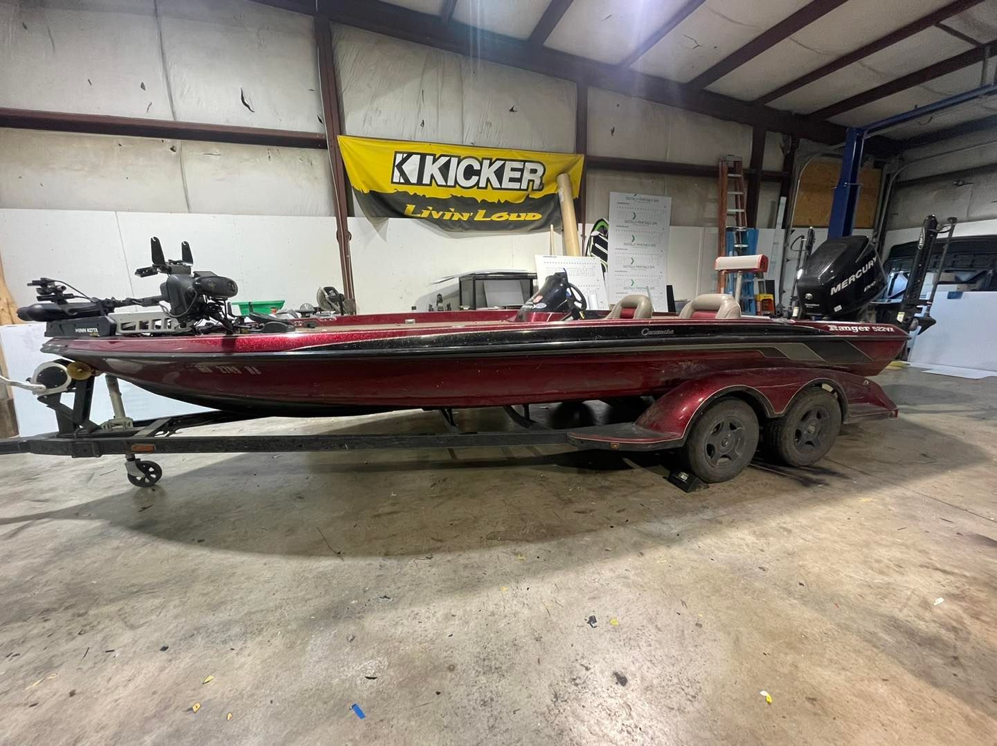 Red fishing boat on a trailer inside a workshop, with a Kicker banner in the background.