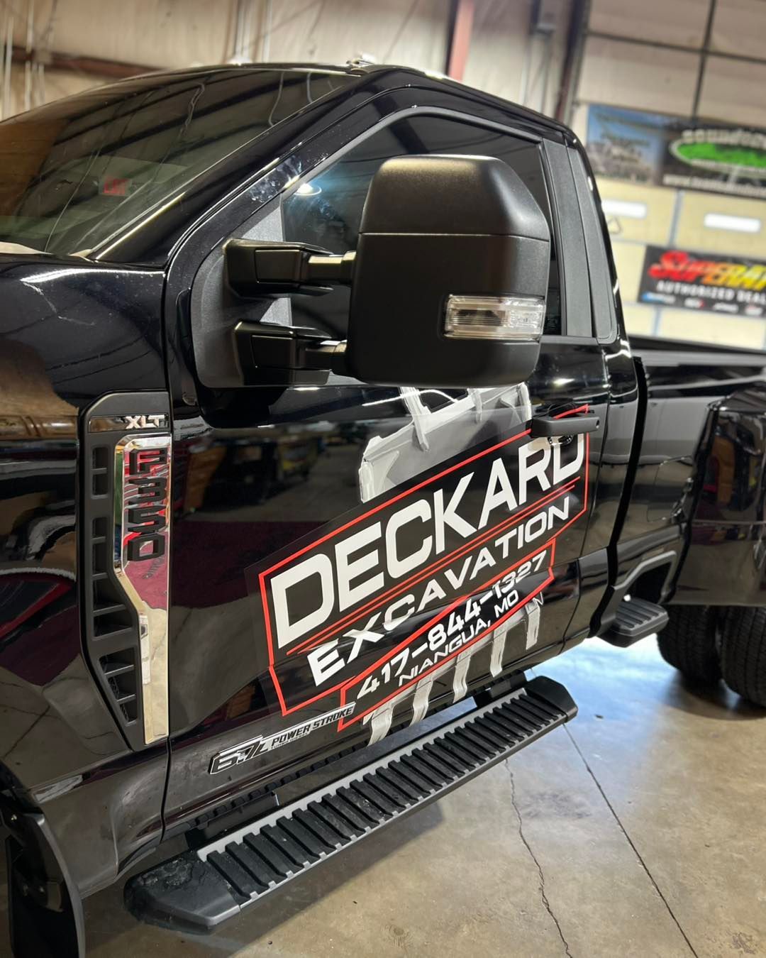 Black pickup truck with “DECKARD EXCAVATION” logo parked indoors at a shop or garage.