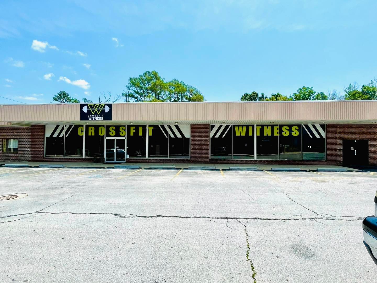 Strip mall storefront for CrossFit and fitness gym with black awnings and large windows under a blue sky