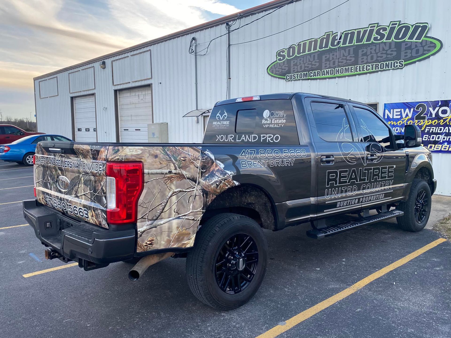 Black pickup truck with camo rear panels parked outside a building