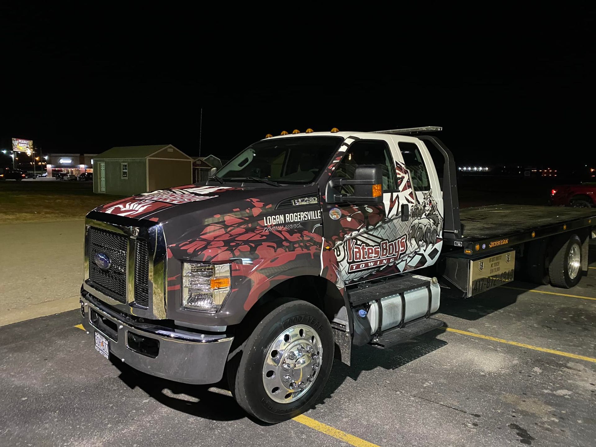 Customized flatbed tow truck with red and black graphics parked at night in a parking lot