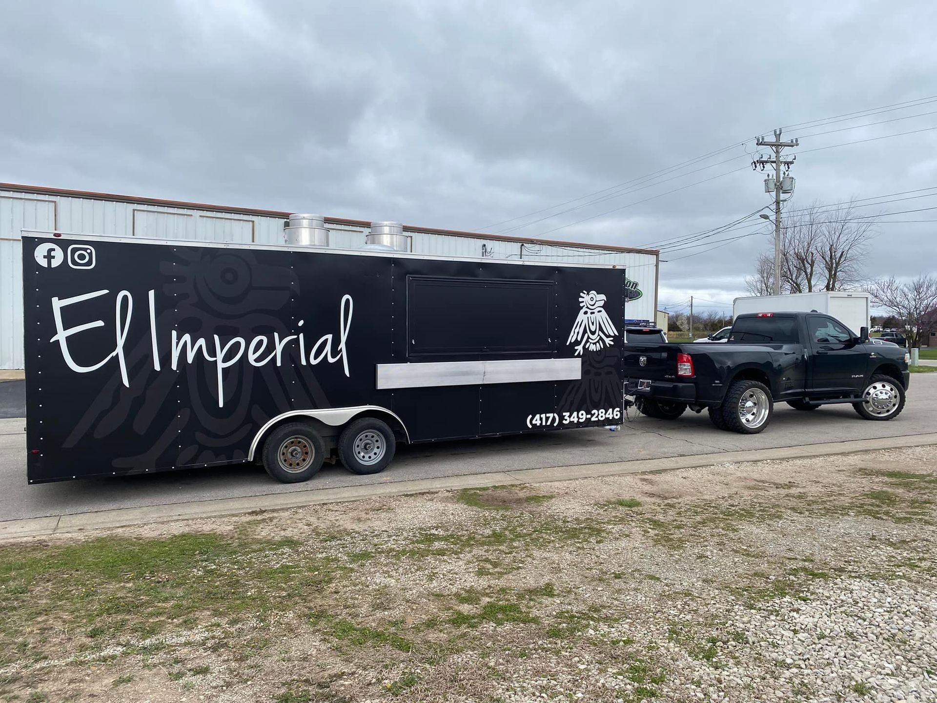 Black food trailer labeled “El Imperial” hitched to a black truck in a cloudy lot