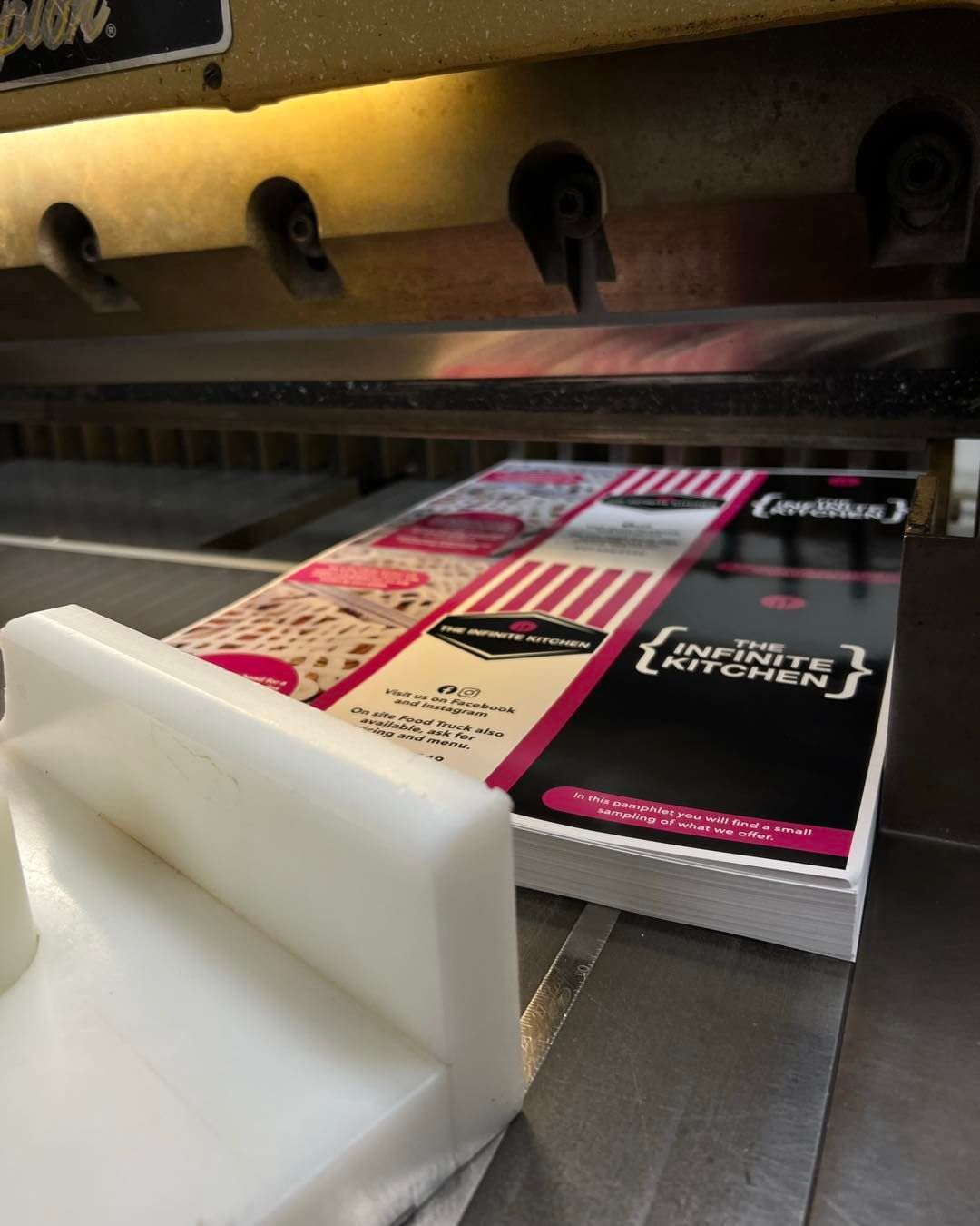 Printed cards being cut on a machine, with white guides in the foreground and colorful stacks on the tray