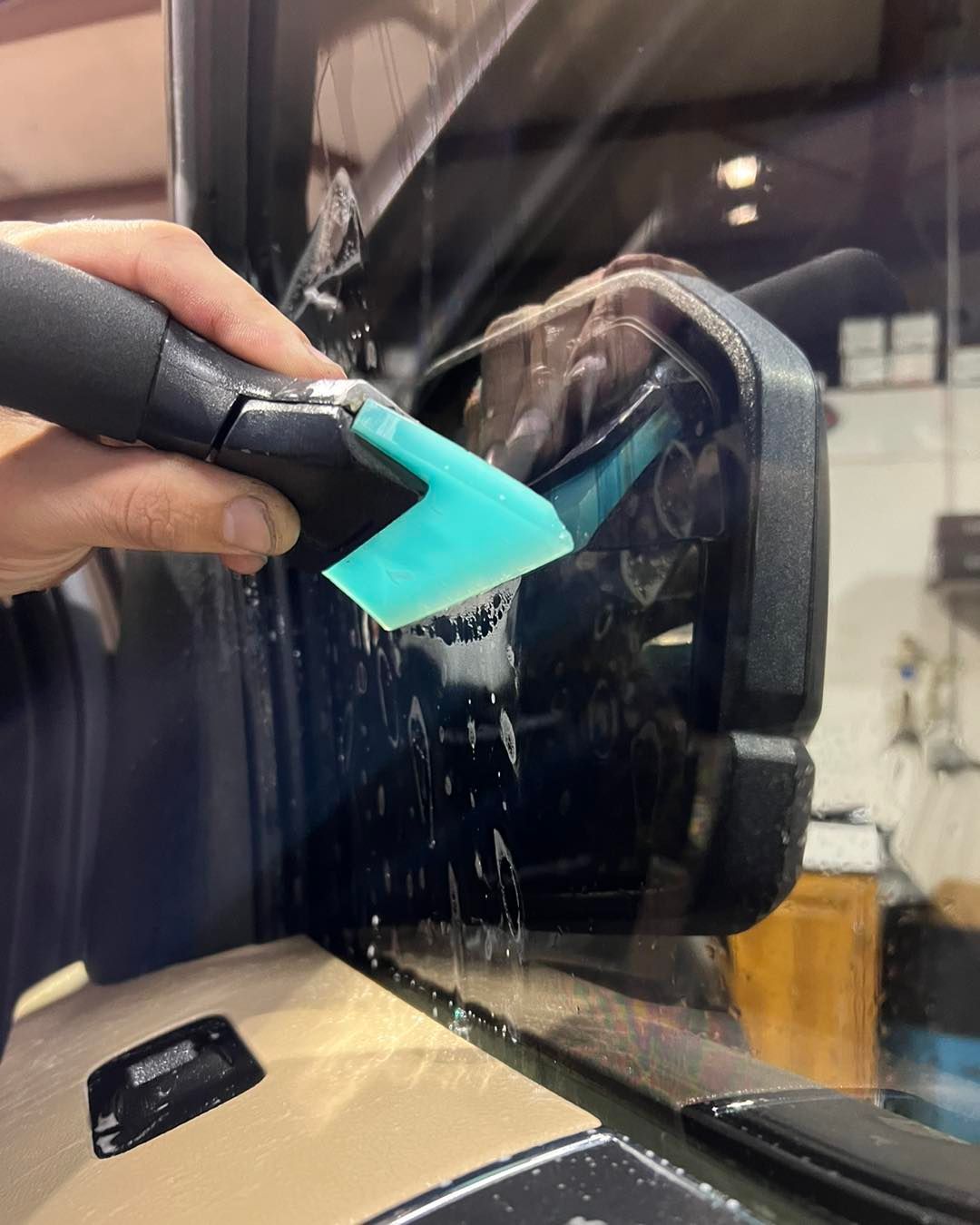 Hand using a teal squeegee to clean water off a car window or windshield