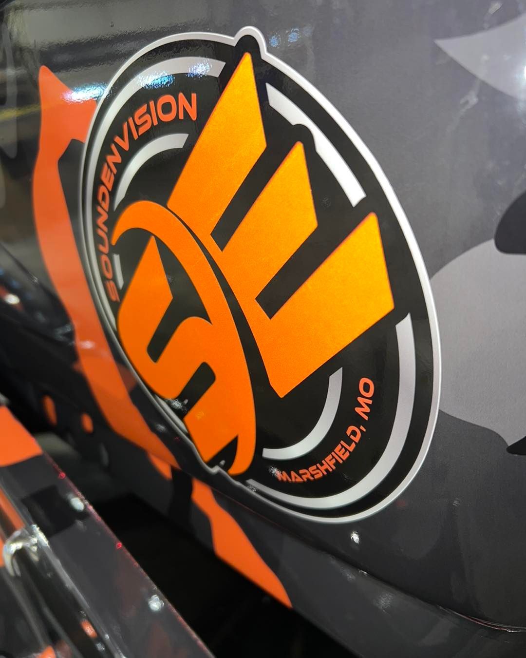 Orange and black circular logo decal on a glossy dark vehicle panel