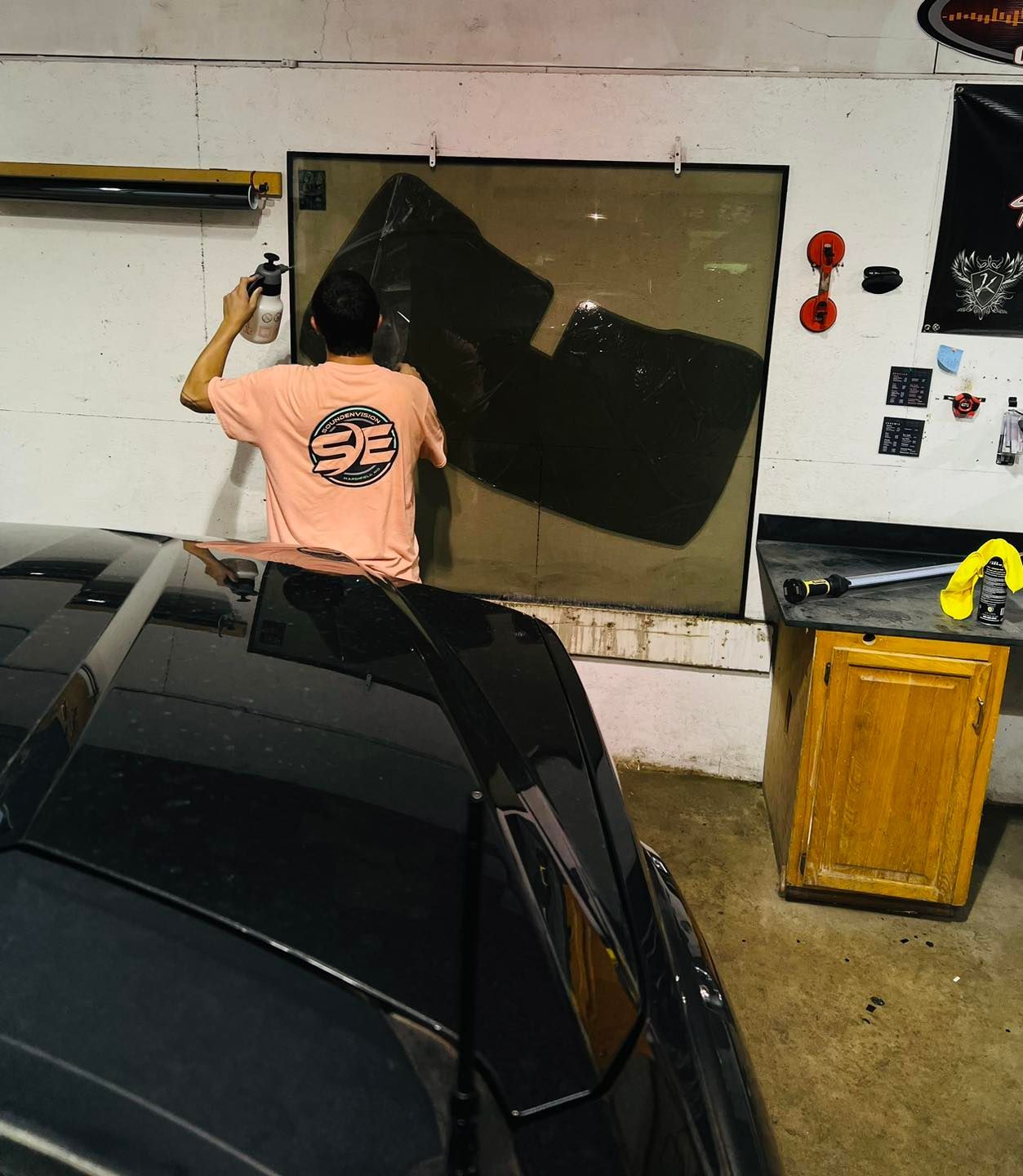 Person applying dark film to a car window in a garage workshop