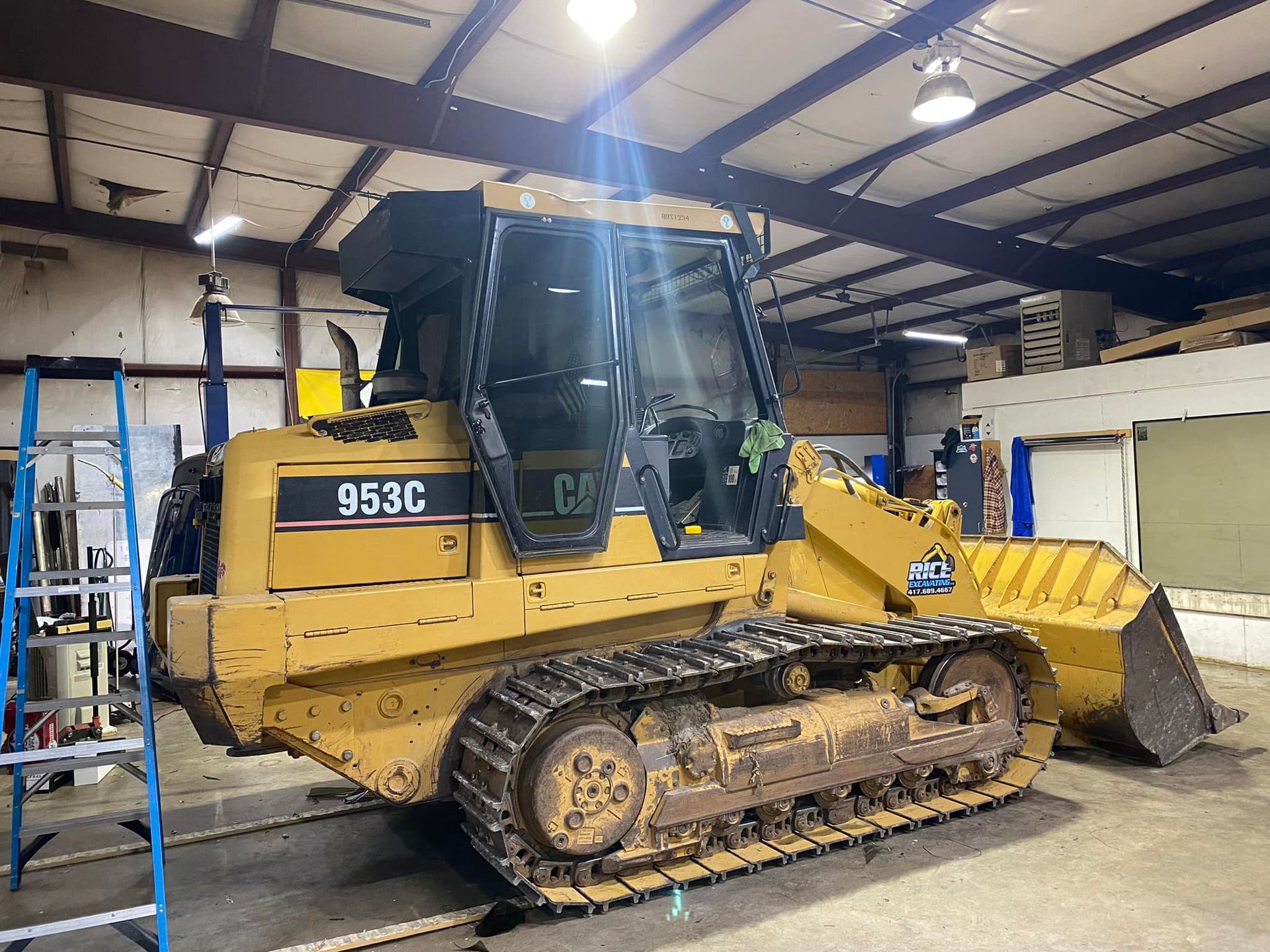 Yellow Caterpillar 953C tracked loader in a warehouse, side view with bucket raised slightly.