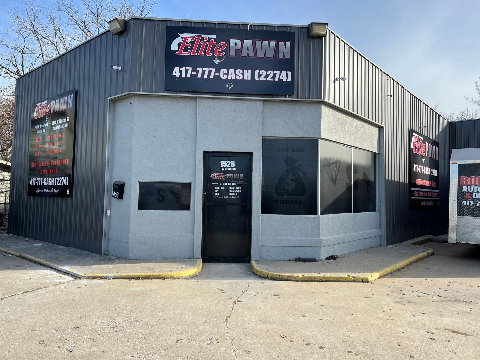 Pawn shop storefront with blue-gray siding and black signs on a sunny corner lot