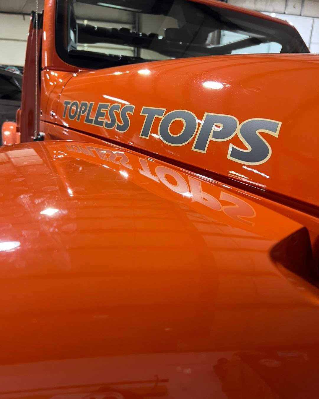 Orange vehicle with “TOPLESS TOPS” lettering on the side in a garage