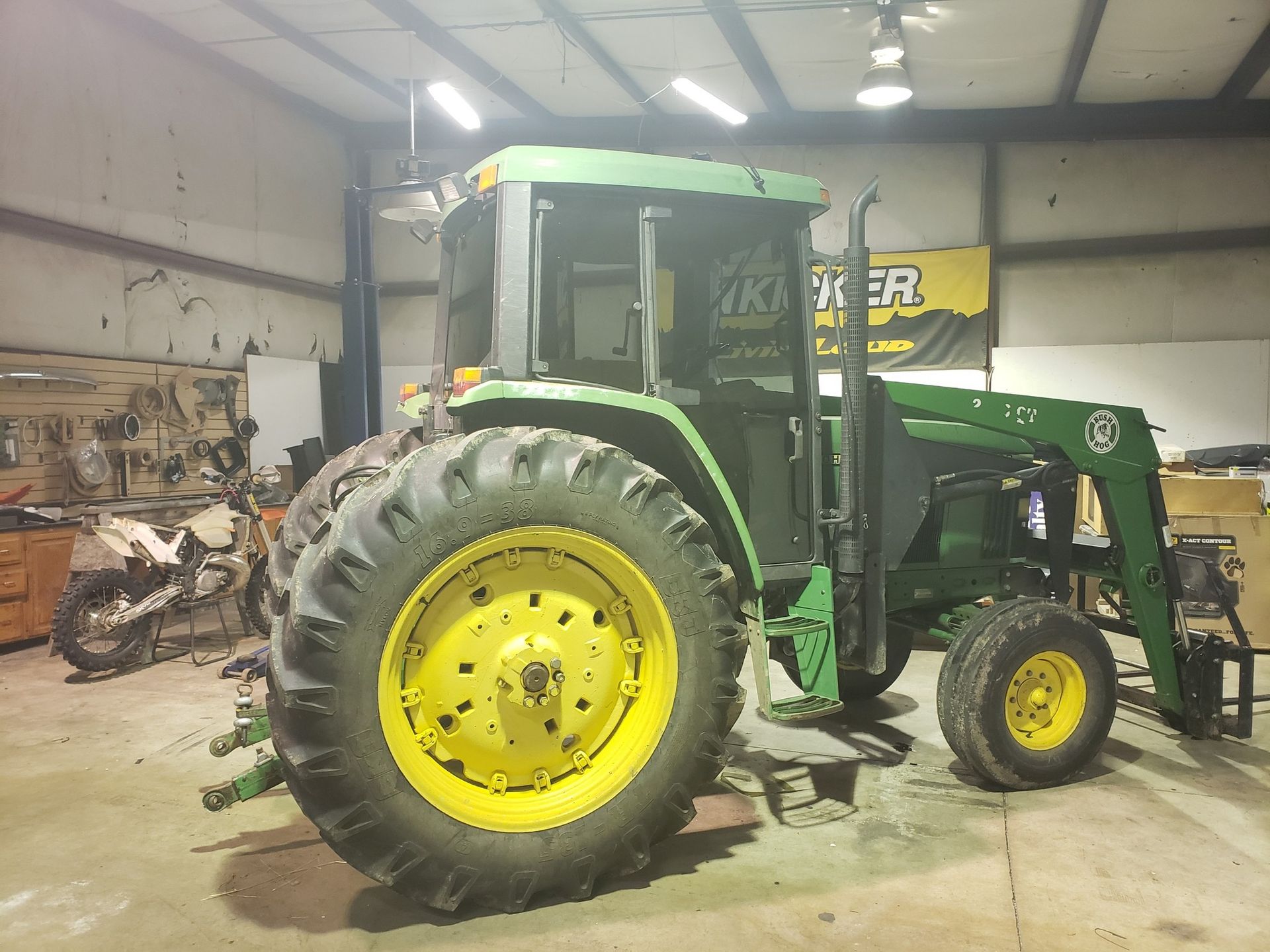 Green John Deere tractor with yellow wheels parked inside a garage or workshop.