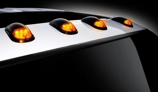 Close-up of a white vehicle roof with four amber marker lights on a black background