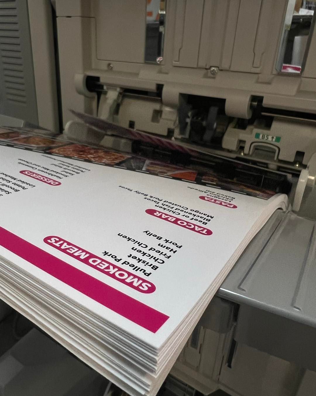 Stack of white printed flyers on a machine with magenta labels in an office or print shop