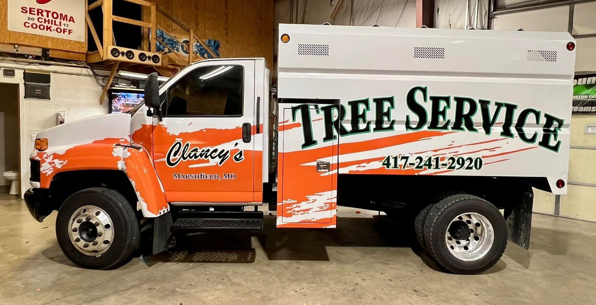 Orange and white tree service truck parked indoors with large TREE SERVICE lettering on the side