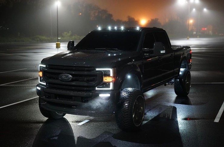 Black Ford pickup truck in a wet, foggy parking lot at night with headlights on