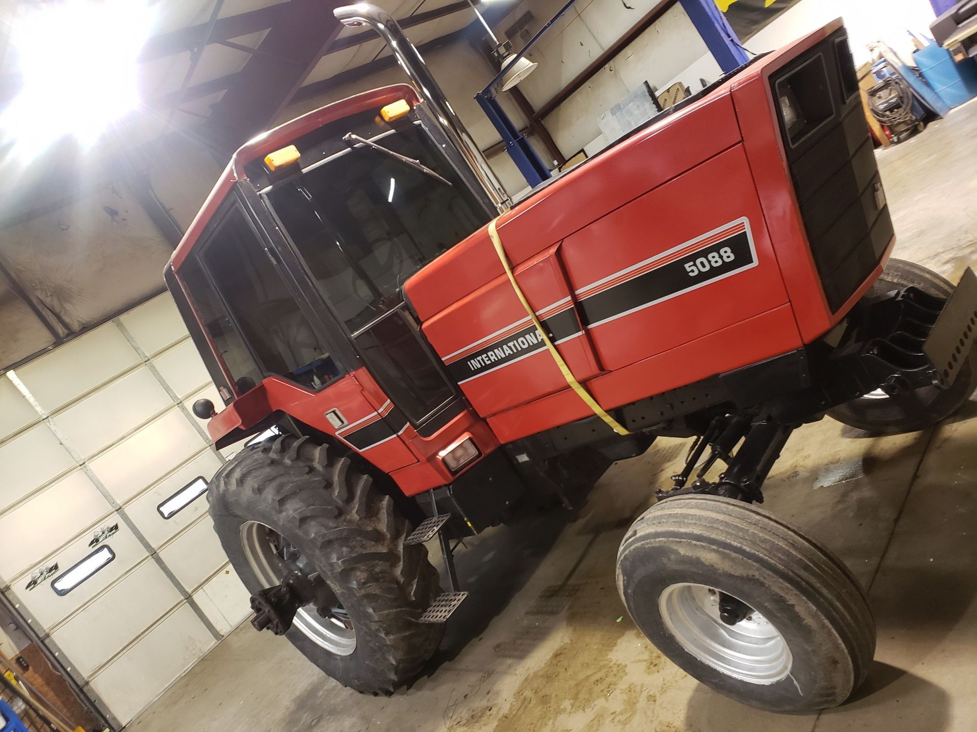 Red farm tractor with front wheel removed, parked inside a garage or workshop.