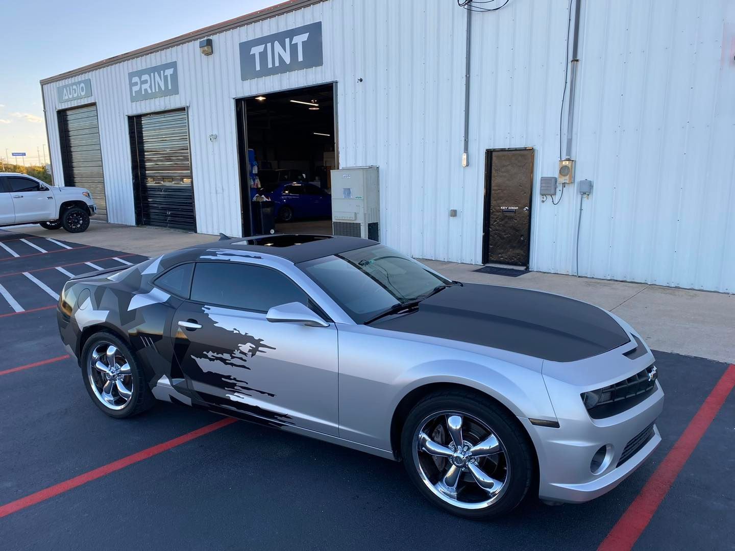 Silver and black sports car parked outside a tint shop with open garage bays