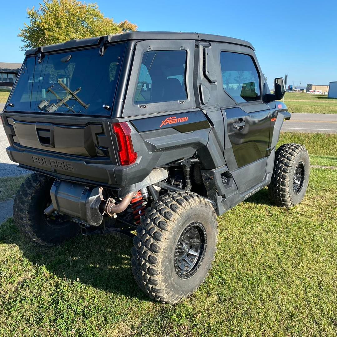 Black lifted off-road side-by-side parked on grass under a clear blue sky.
