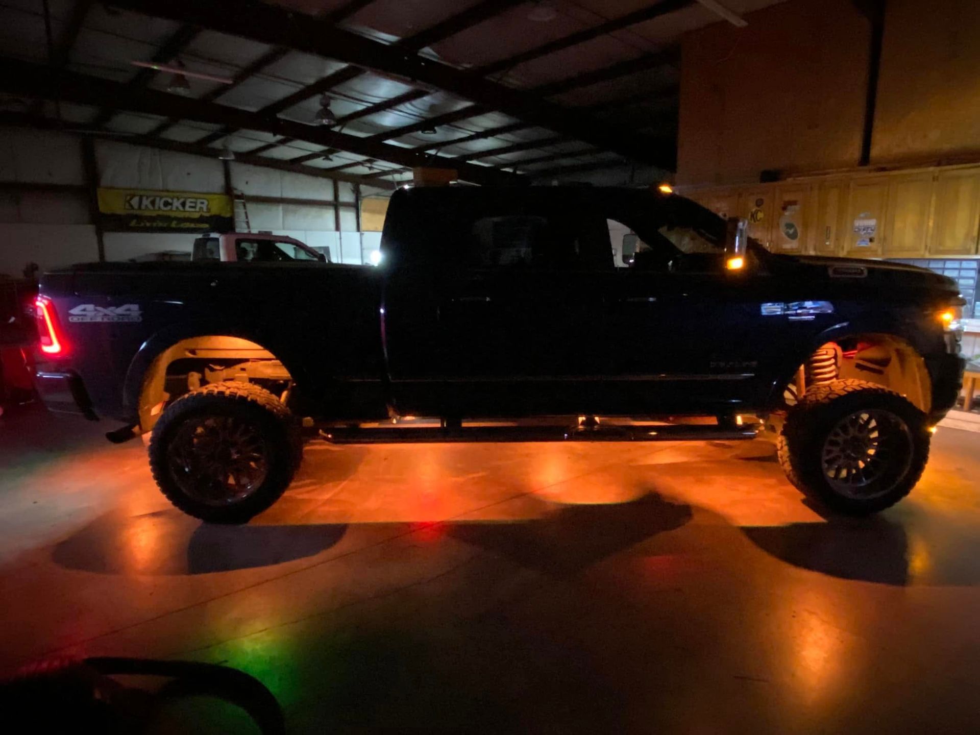 Black lifted pickup truck in a garage, lit by orange reflections on the floor.