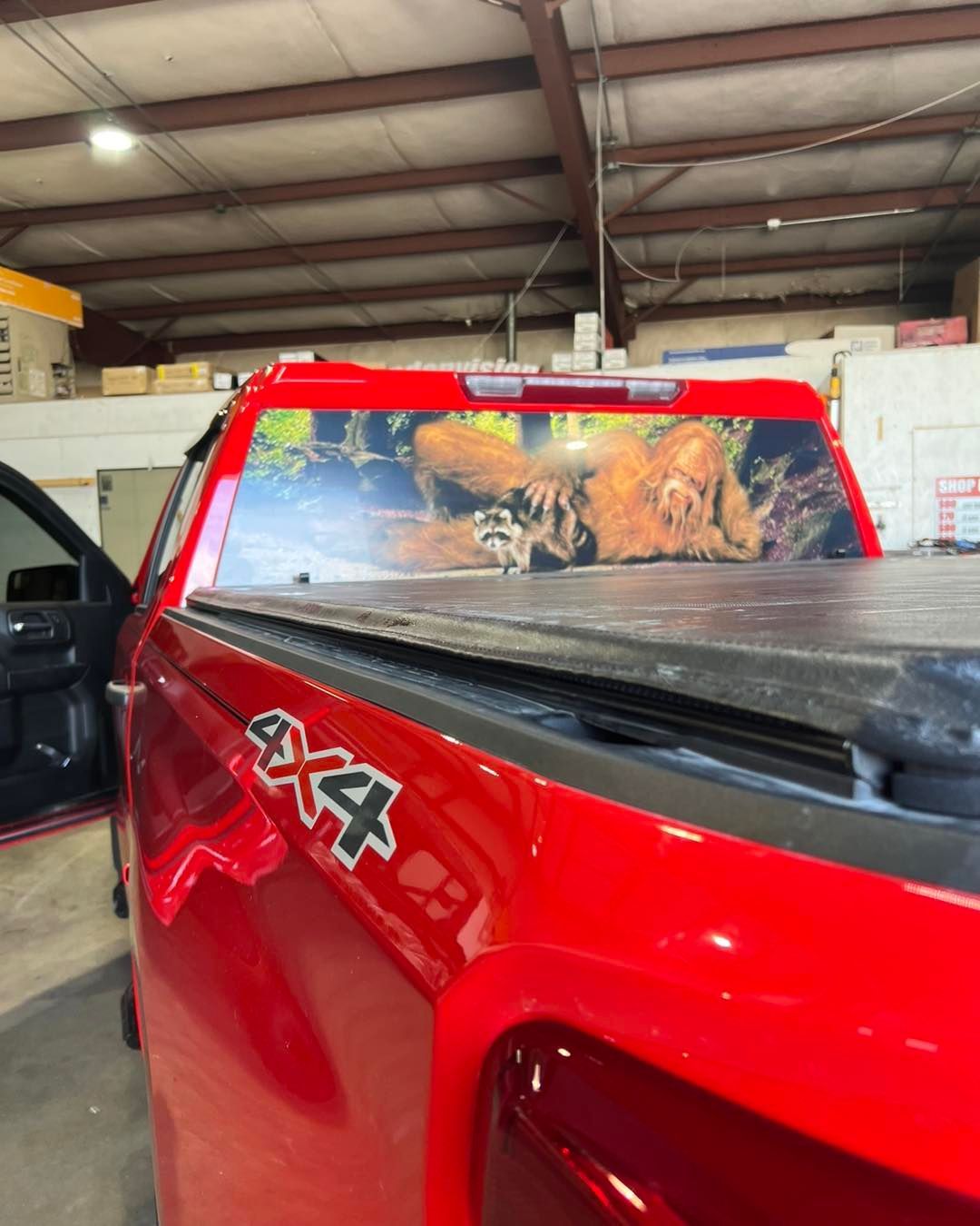 Red pickup truck in a garage, with a dog lying in the truck bed under a painted rear window panel