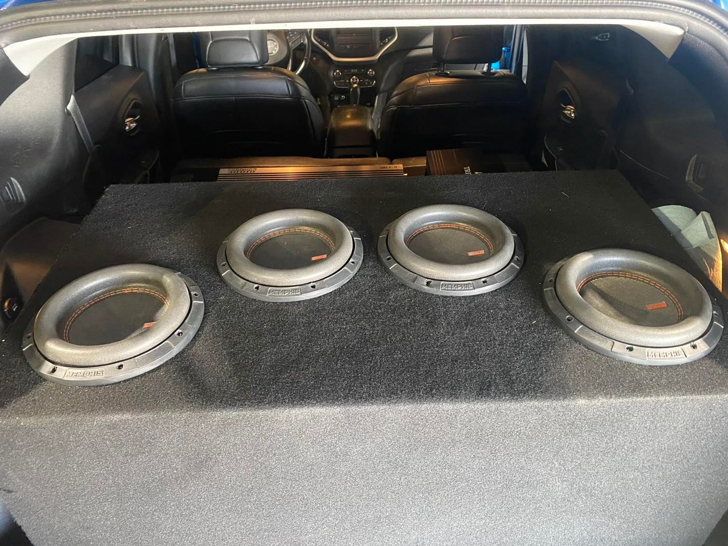 Car trunk with a large subwoofer box and four exposed speaker cones installed inside.