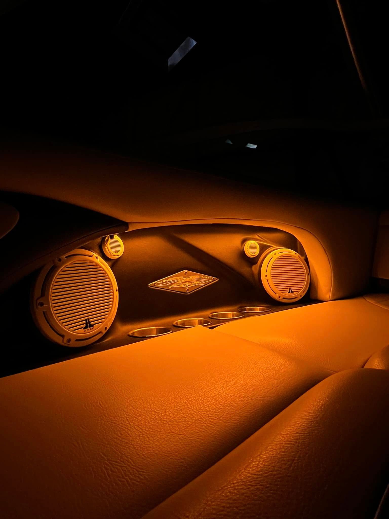 Orange-lit car dashboard and center console at night with speakers and vents