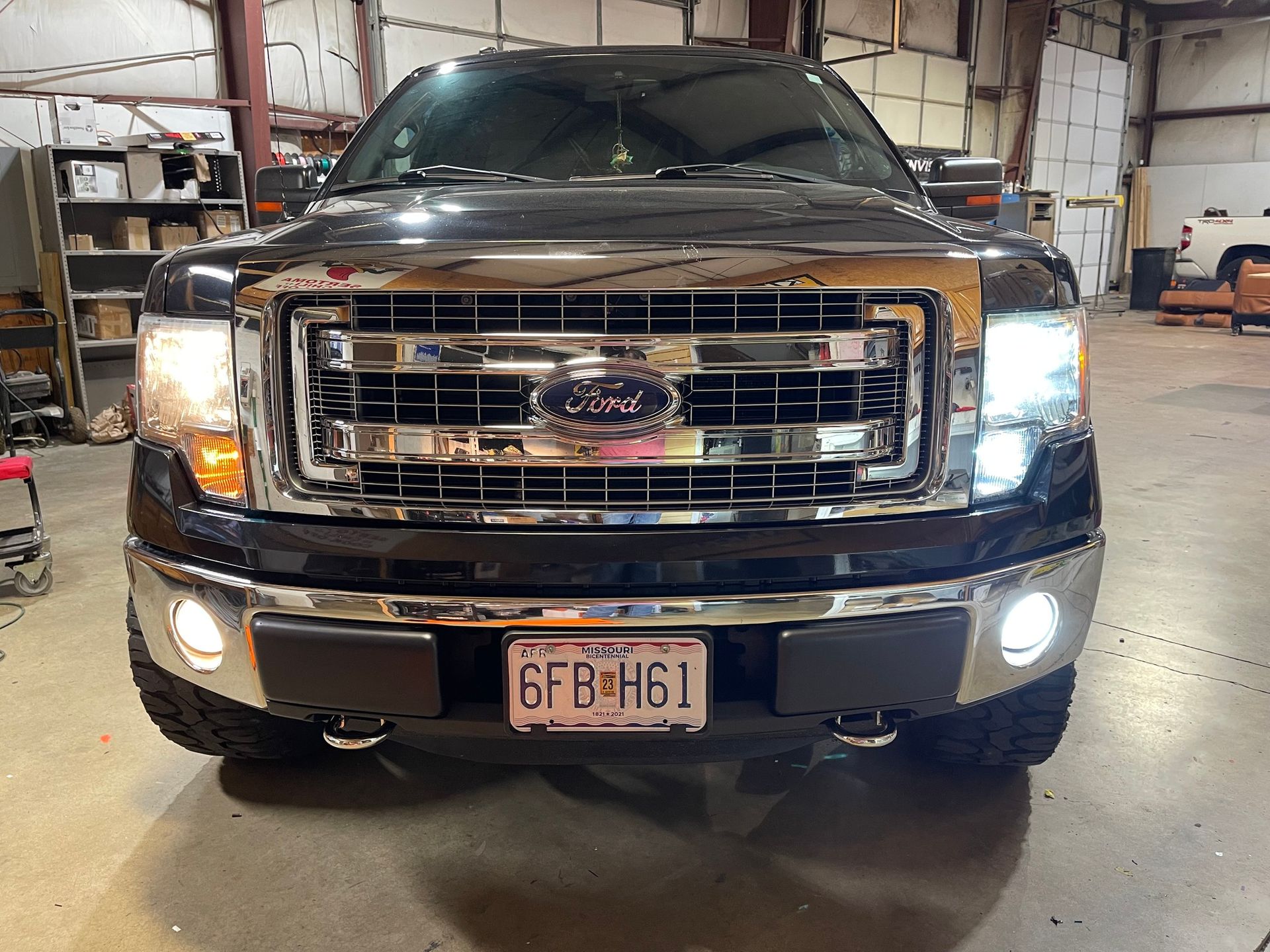 Front view of a black Ford pickup truck in a garage, with headlights on.