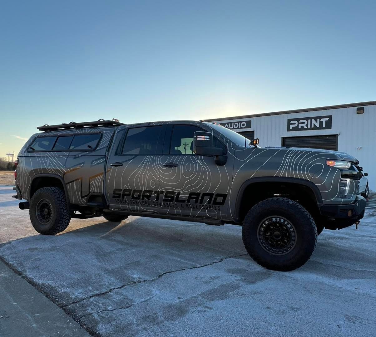 Camouflaged black Sportland pickup truck parked outdoors at dusk.