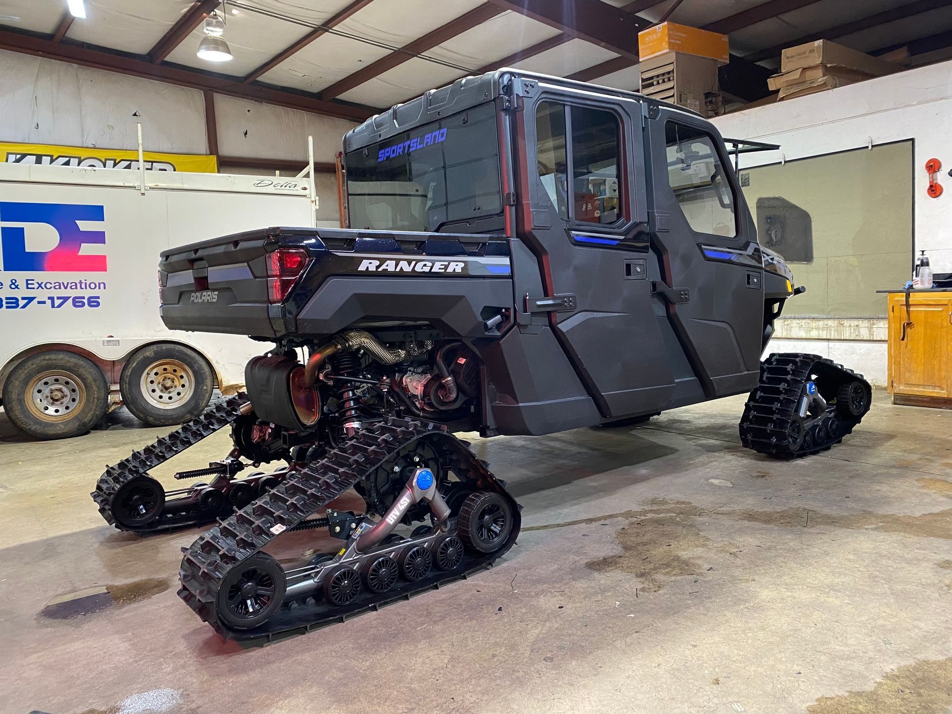 Modified black off-road utility vehicle with tracked wheels inside a garage workshop