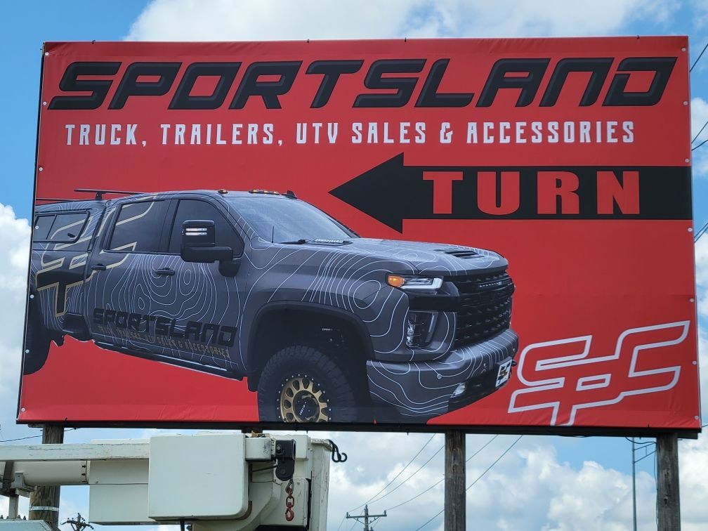 Red Sportsman sign with truck graphic and “TRUCK, TRAILERS, UTV SALES & ACCESSORIES” text over a red background