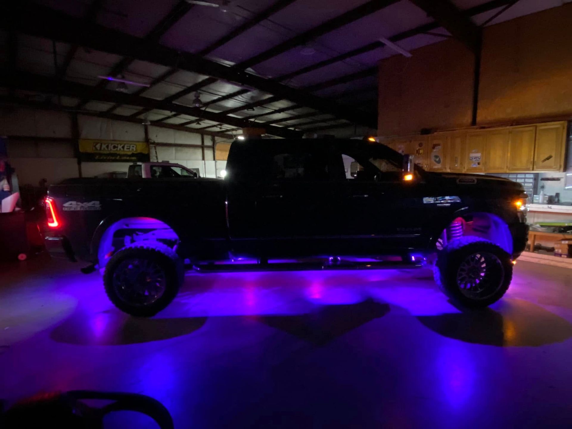Black pickup truck with purple underglow parked inside a dim warehouse at night