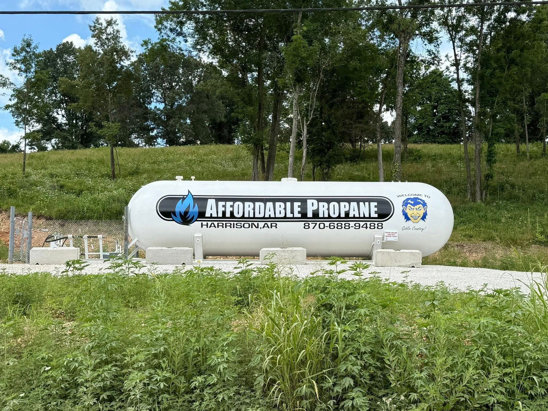 Large white propane tank labeled “Affordable Propane” beside grass and trees outdoors