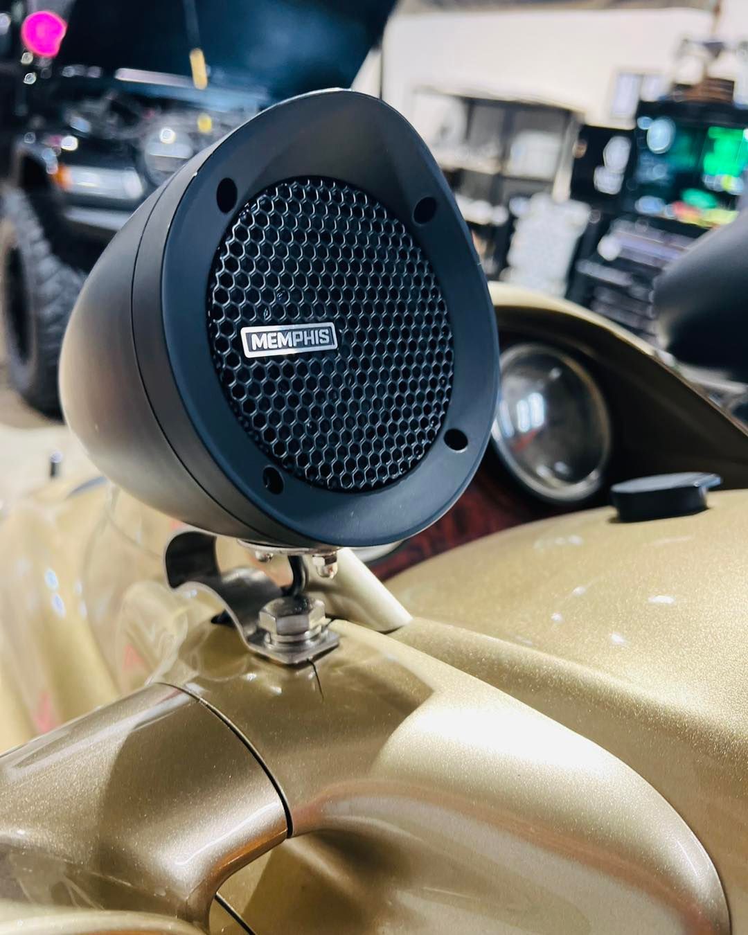 Black round speaker mounted on a gold car hood at an auto show.