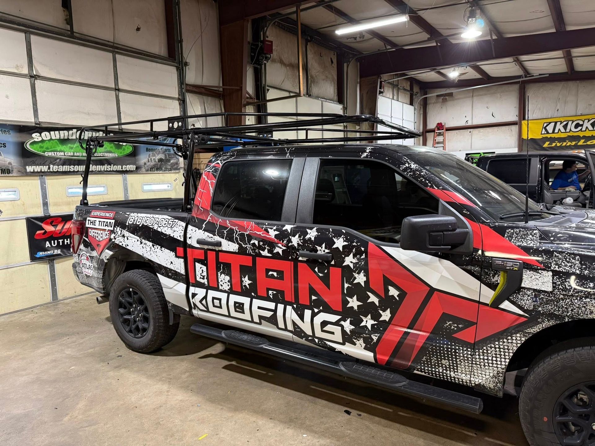 Black Titan Roofing pickup truck wrapped in red and white graphics inside an auto shop