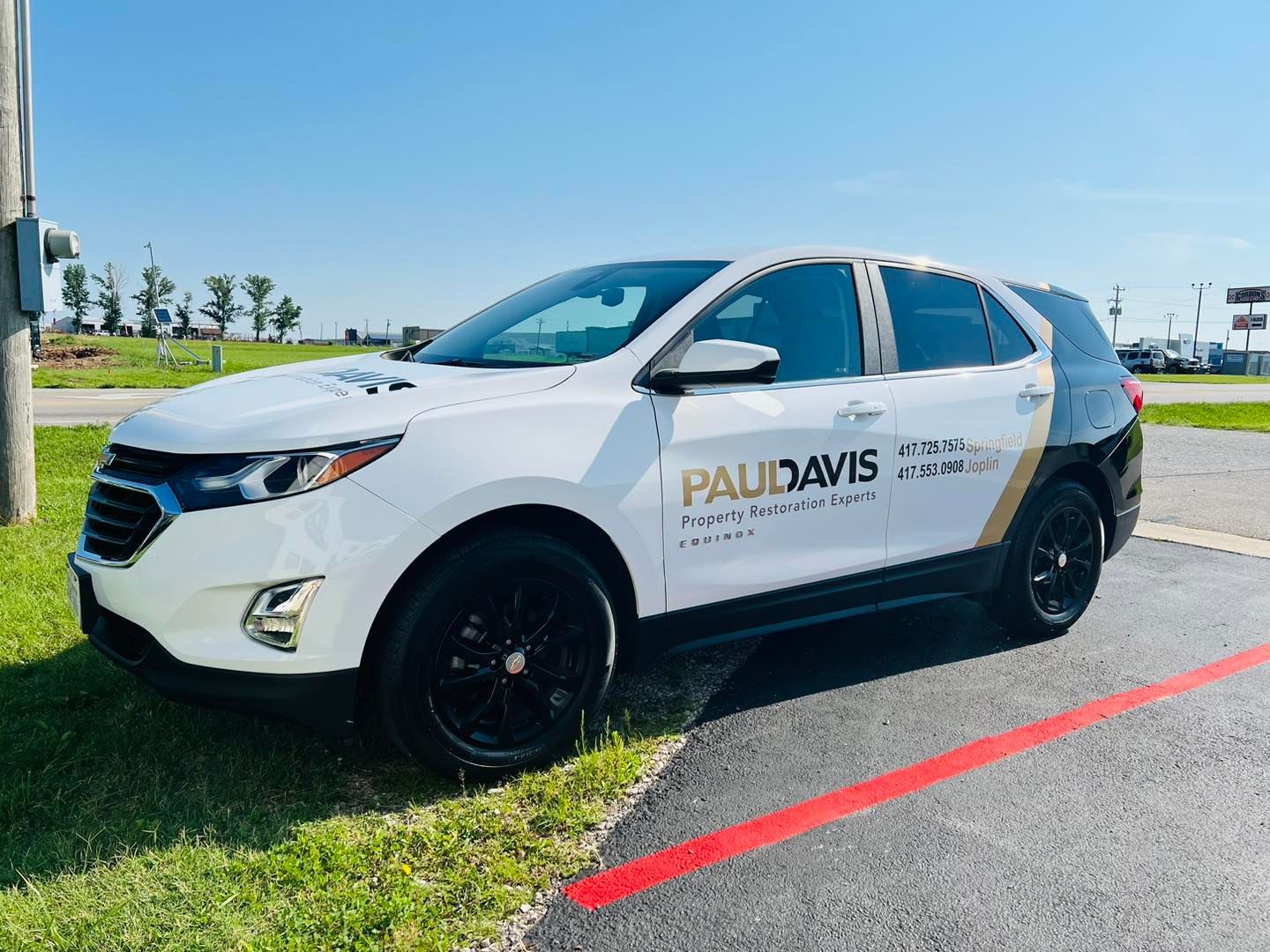 White and black Paul Davis service SUV parked on grass by a roadside under a clear blue sky