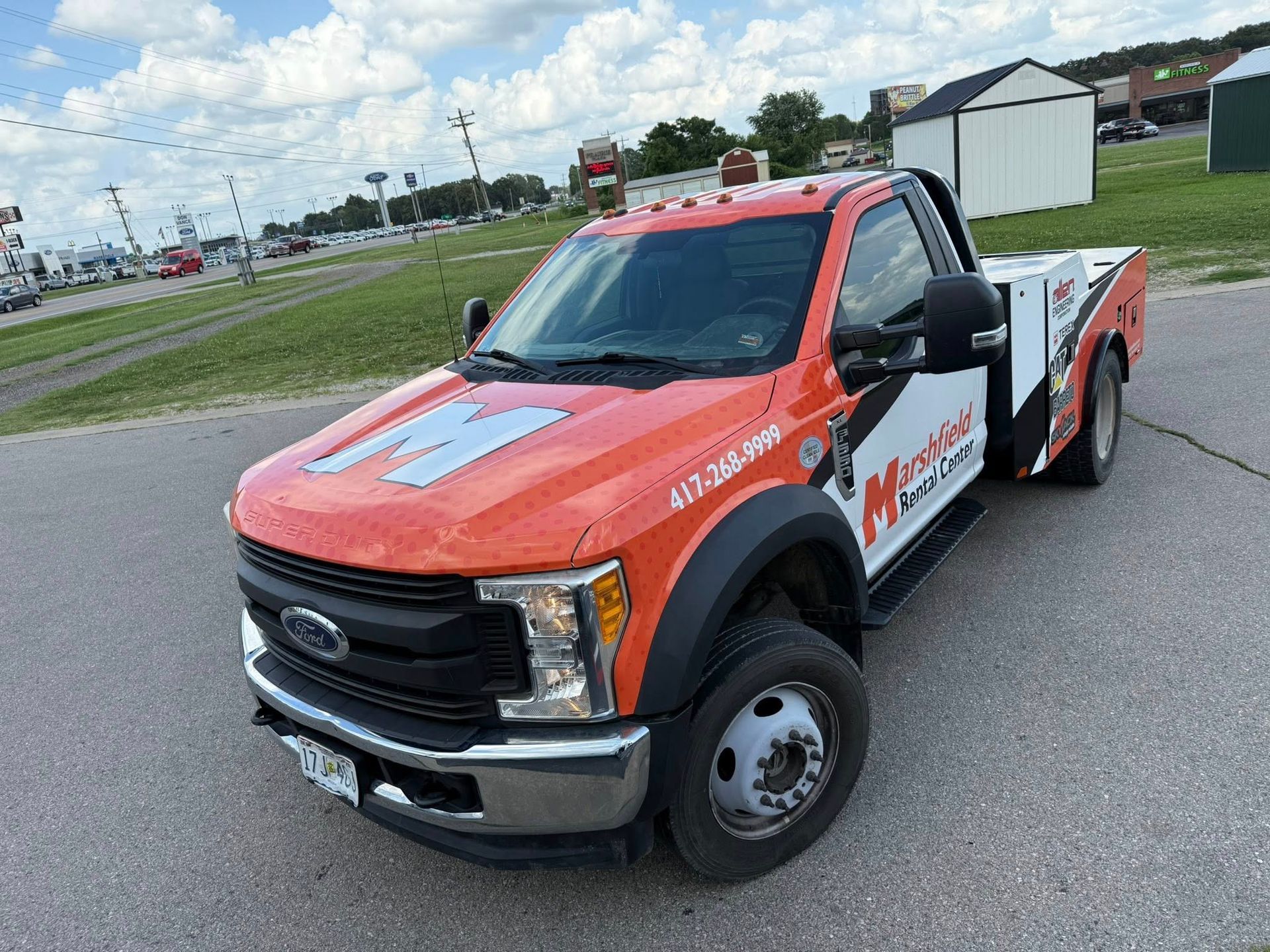 Orange and white tow truck parked on a road near a grassy lot under a cloudy sky