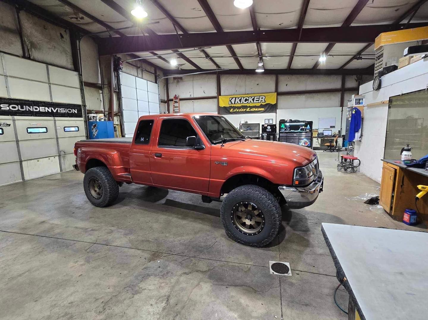 Red lifted pickup truck in a garage workshop, viewed from the side.
