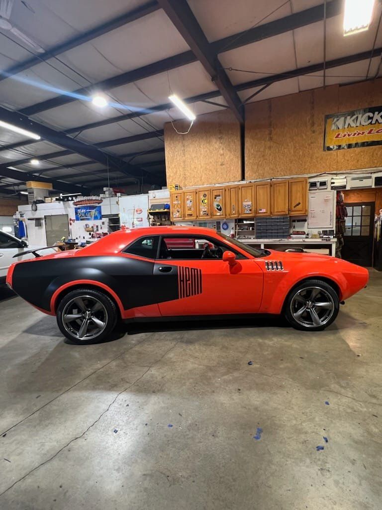 Red and black muscle car parked inside a garage with cabinets and tools in the background