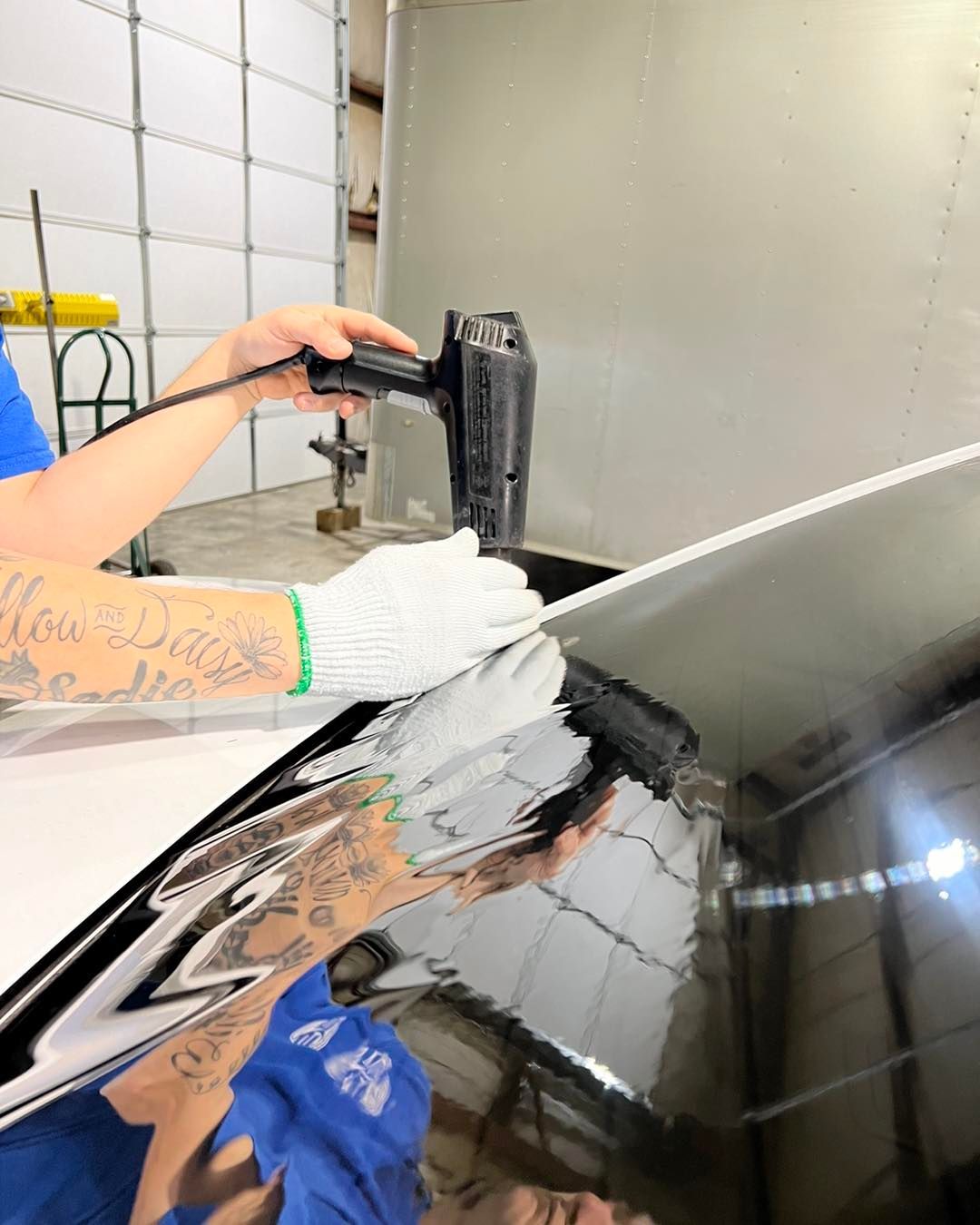 Worker wearing white gloves applying material to a black car surface in a workshop