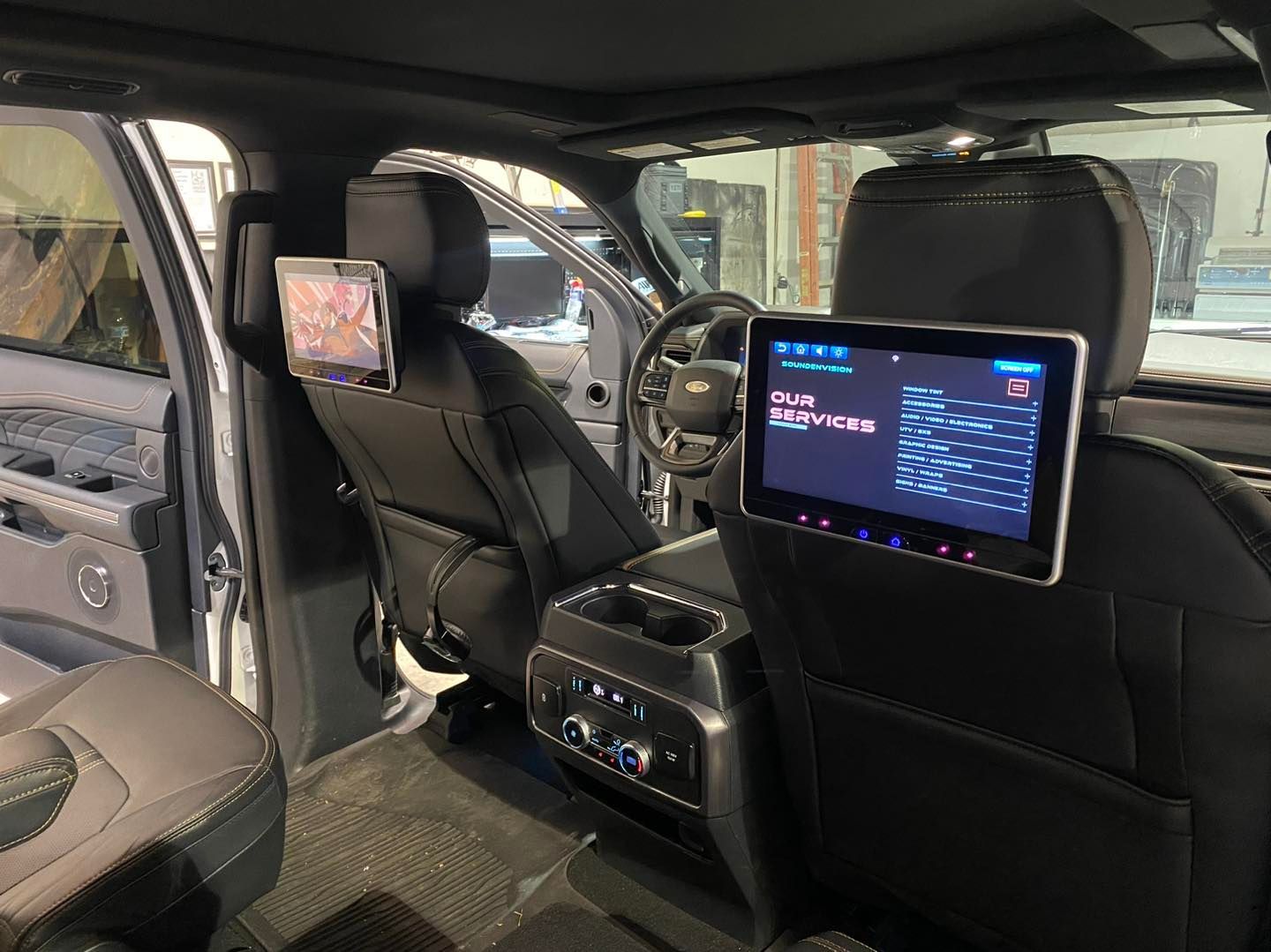 SUV interior with black seats, two rear entertainment screens, and a center console display