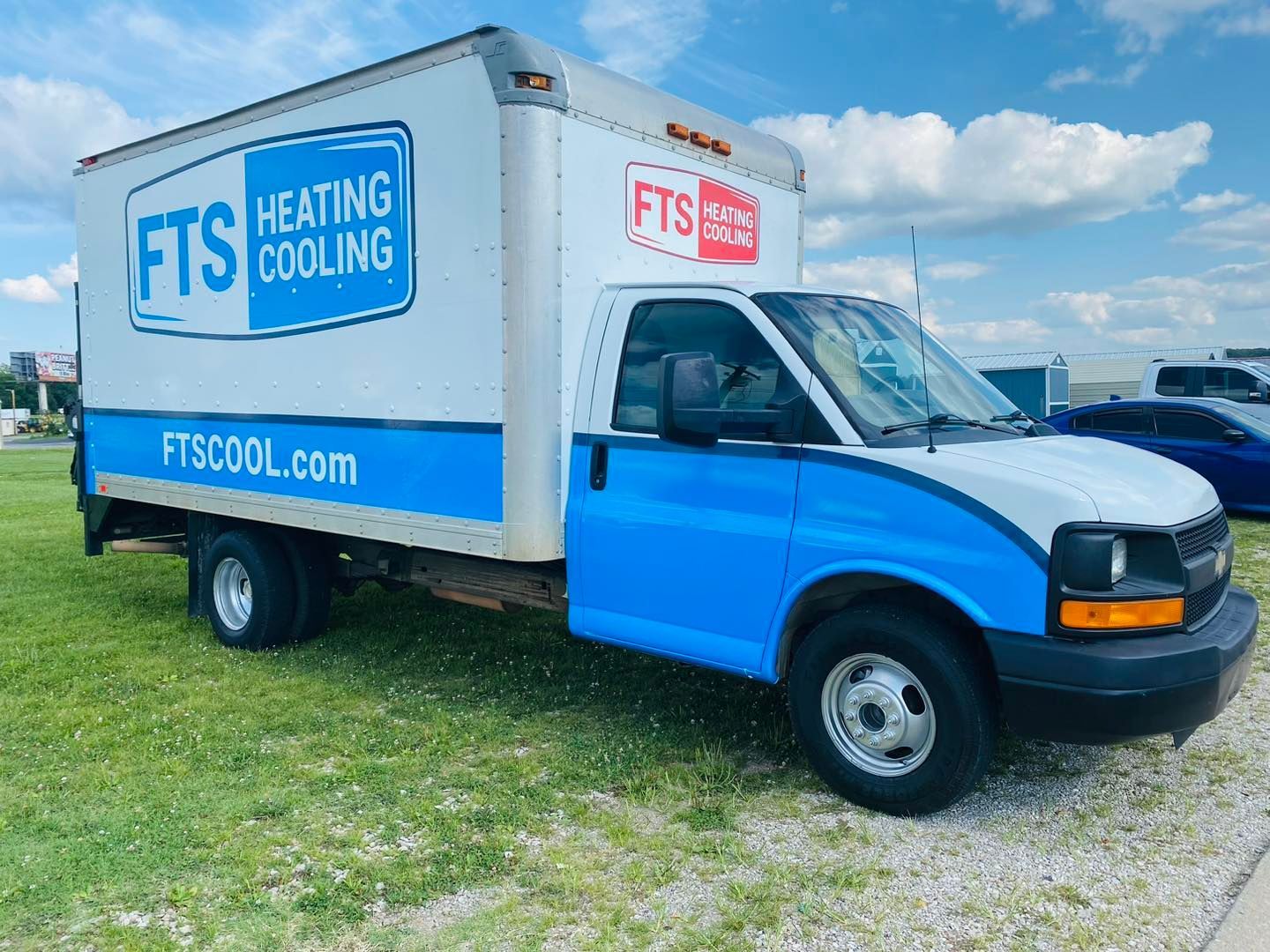 Blue FTS Heating Cooling box truck parked on grass under a cloudy sky