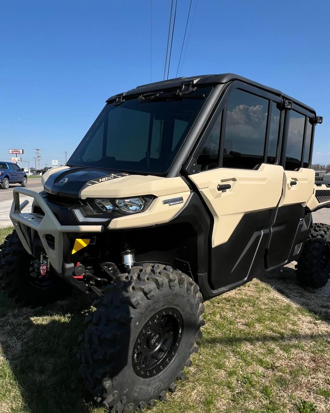 Beige and black off-road side-by-side ATV with large tires parked on grass under a clear blue sky