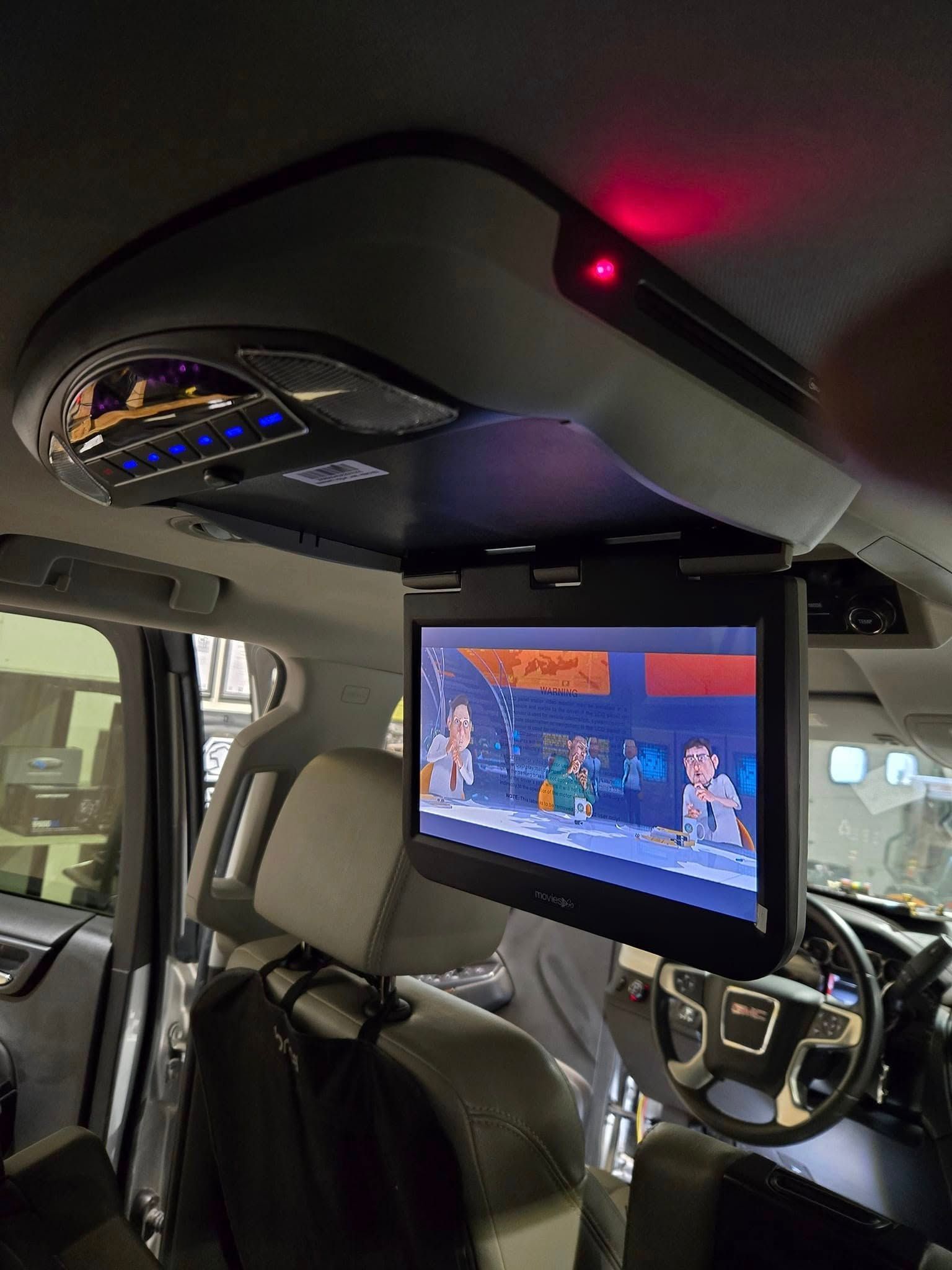 Car interior with a mounted screen showing a video game and a red LED light on the ceiling console