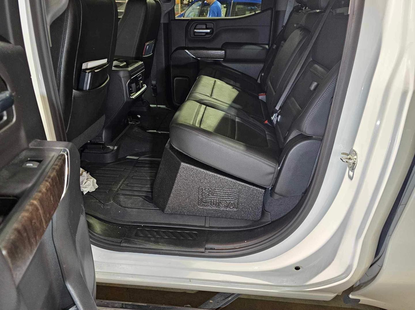 Open car door showing black leather back seat and dark floor mats inside a white vehicle.