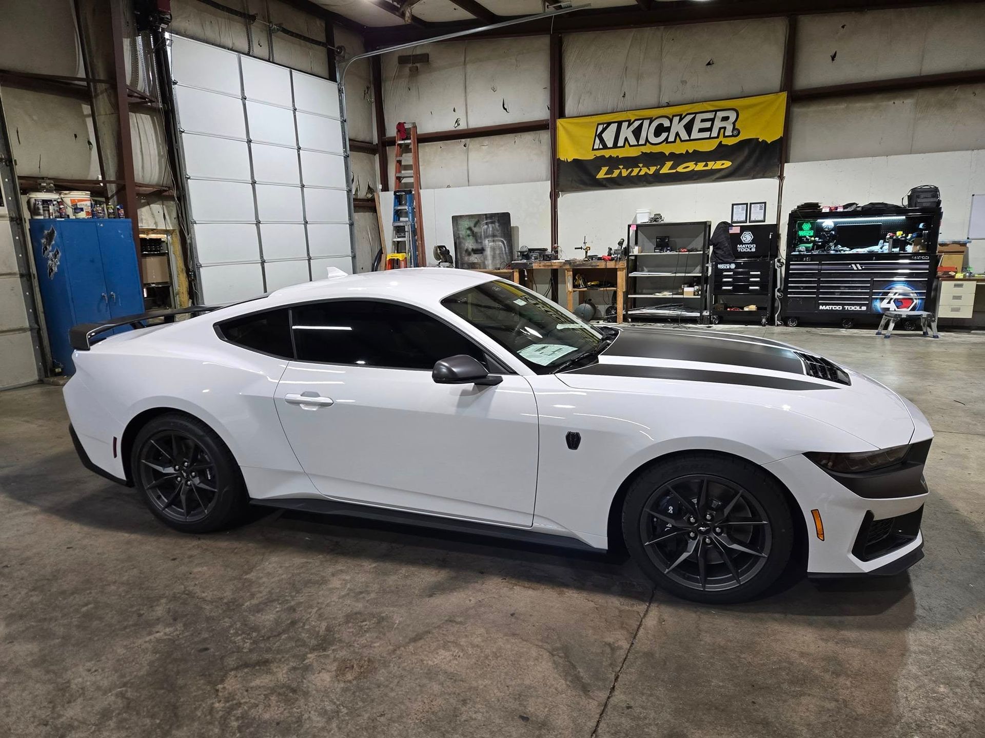 White sports car in a garage, side view with black hood and wheels, racing shop background